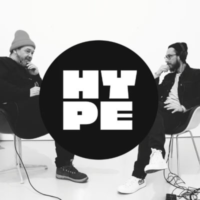 Zwei Männer sitzen sich gegenüber und unterhalten sich, in der Mitte sieht man ein schwarzes Logo mit der Aufschrift &quot;HYPE&quot;