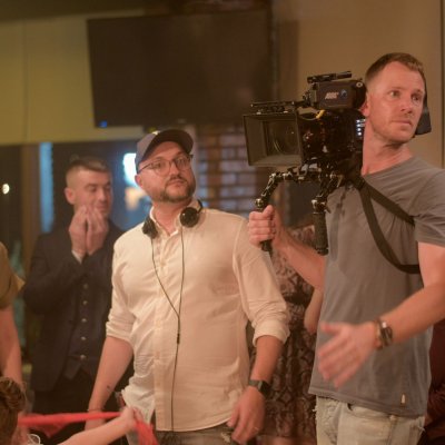 Regisseur und Kameramann am Filmset, umgeben von mehreren Personen