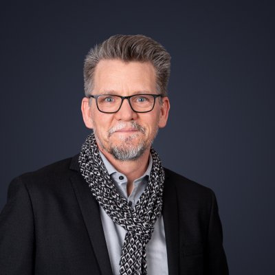 ThomasFabich Thomas Fabich steht vor einem dunklen Hintergrund und guckt in die Kamera