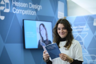 Frau schaut in Kamera mit Flyer zu Hessen Design Competition in der Hand