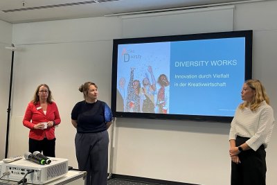 drei Frauen stehen auf einer Bühne vor einem Screen