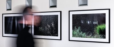 Eine verschwommene Person steht vor einer Wand an der drei Bilder hängen