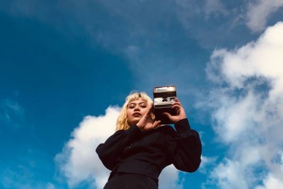 Frau mit Kamera vor blauem Himmel stehend Frau mit Kamera vor blauem Himmel stehend